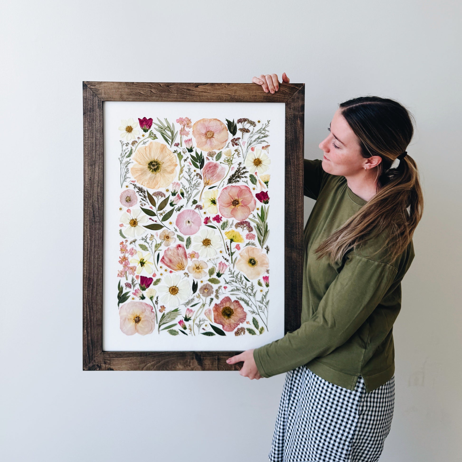 Person holding a framed floral artwork against a white wall
